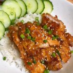 honey soy chicken on a plate of rice with cucumbers