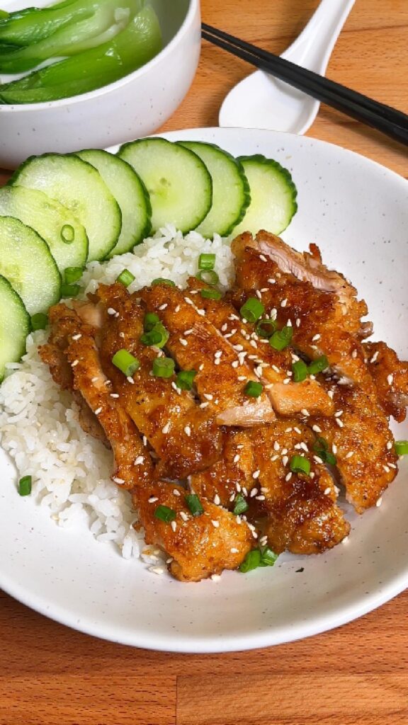 honey soy chicken on a plate of rice with cucumbers
